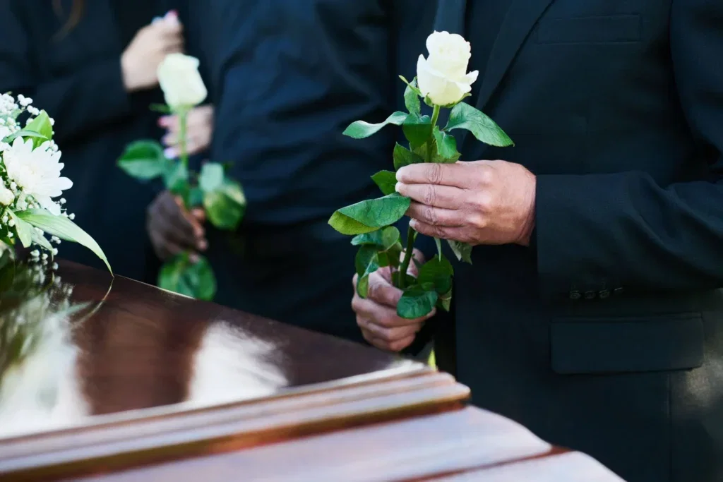 Mourners laying white roses on a coffin.