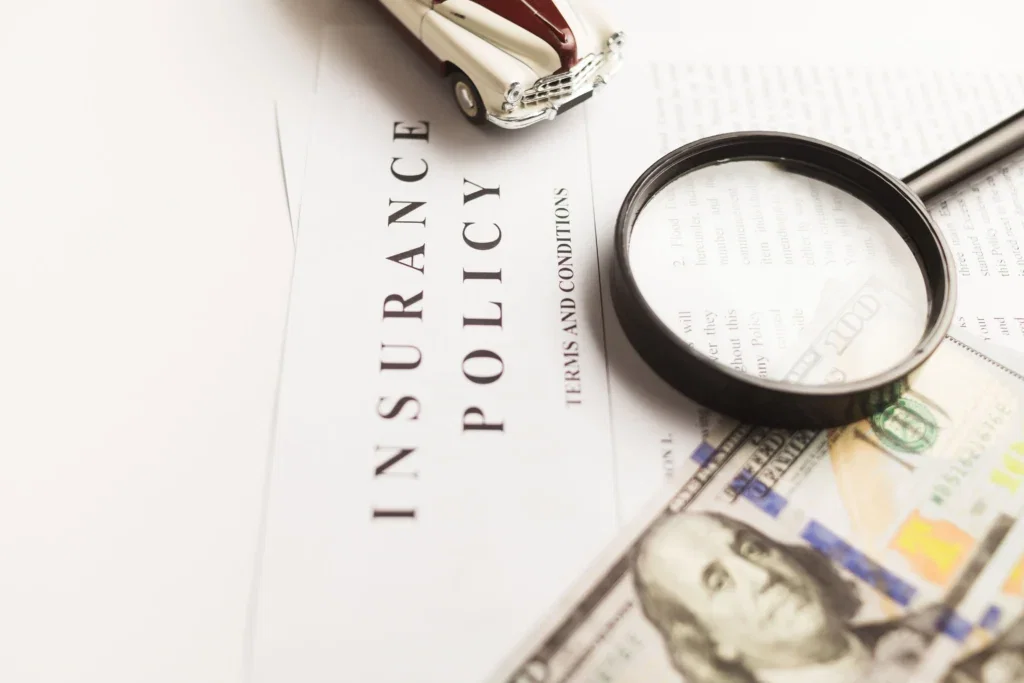 Close-up of a small toy car placed on a newspaper beside a magnifying glass and scattered dollar bills, implying financial or insurance adjuster trick scrutiny of cars or markets.