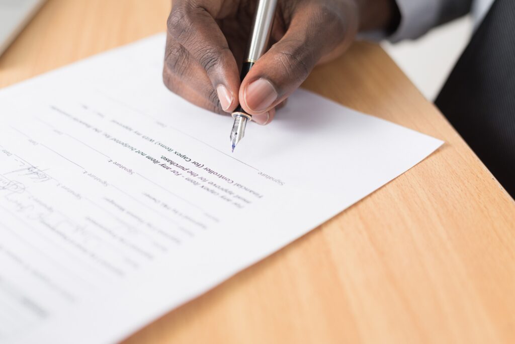 A hand signing a contract, illustrating that the answer to the question “can a personal injury lawyer drop your case?” is yes.